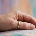Bague pouce femme signification : bien plus qu'un style 5 Close-up of a relaxed female hand with a gold thumb ring, against a soft, blurred background of muted lavender, peach, and teal.