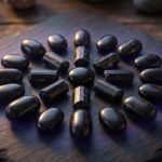 Pierres noires signification : révélez votre force 3 A balanced arrangement of polished black Tourmaline, Obsidian, and Onyx stones on dark slate with a subtle indigo glow, conveying protection and grounding. Soft light highlights their textures on a blurred wooden background.