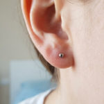 Prothèse boucle d'oreille : réussir sa cicatrisation 3 Close-up of an earlobe with a new, small, metallic medical-grade stud earring. Skin is healthy, showing no irritation, in a healing state.