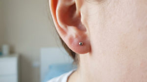 Close-up of an earlobe with a new, small, metallic medical-grade stud earring. Skin is healthy, showing no irritation, in a healing state.