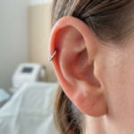 Close-up of a healthy ear with a minimalist silver hoop helix piercing, showing calm skin and a clean, blurred background.