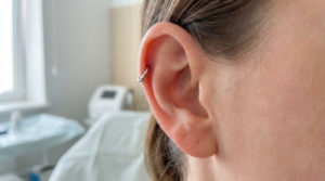 Close-up of a healthy ear with a minimalist silver hoop helix piercing, showing calm skin and a clean, blurred background.