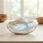 Nacre : vertus insoupçonnées pour corps et esprit 1 A polished, iridescent mother-of-pearl shell on a light stone surface. Blurred spa items and soft natural light create a tranquil scene.