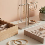 Ranger ses bijoux : mes secrets pour les protéger 3 Diverse gold and silver jewelry, including gemstone rings, necklaces, and earrings, neatly displayed in modern wooden and metallic organizers on a vanity with soft lighting.