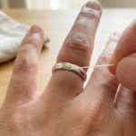 Enlever une bague avec un fil : l'astuce douce et efficace 4 A close-up shows a hand with a tight silver ring on a swollen finger, as a white thread is carefully inserted to aid removal.